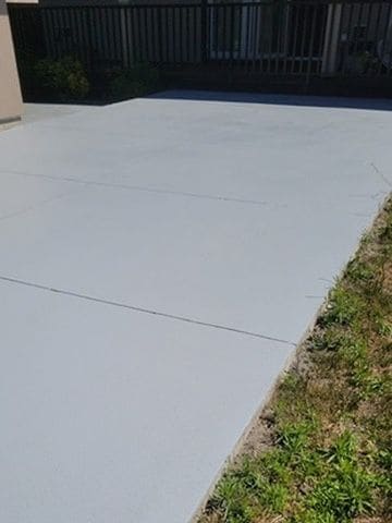 A concrete walkway finished in a smooth light-grey coating, control joints still visible, beside a strip of grass